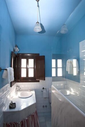 A bathroom with a blue wall, a white sink, a mirror, and a window with shutters. - Cortijo Las Piñas (Tarifa)