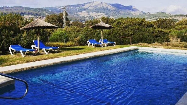 Une piscine à l’eau bleue, entourée de chaises longues bleues et de parasols en chaume.