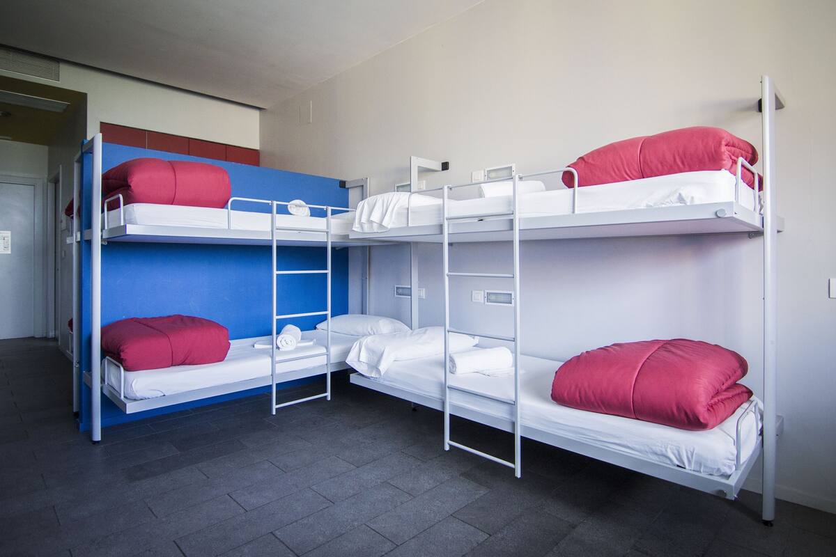 A bunk bed room with three levels, each with a white mattress and red pillows.