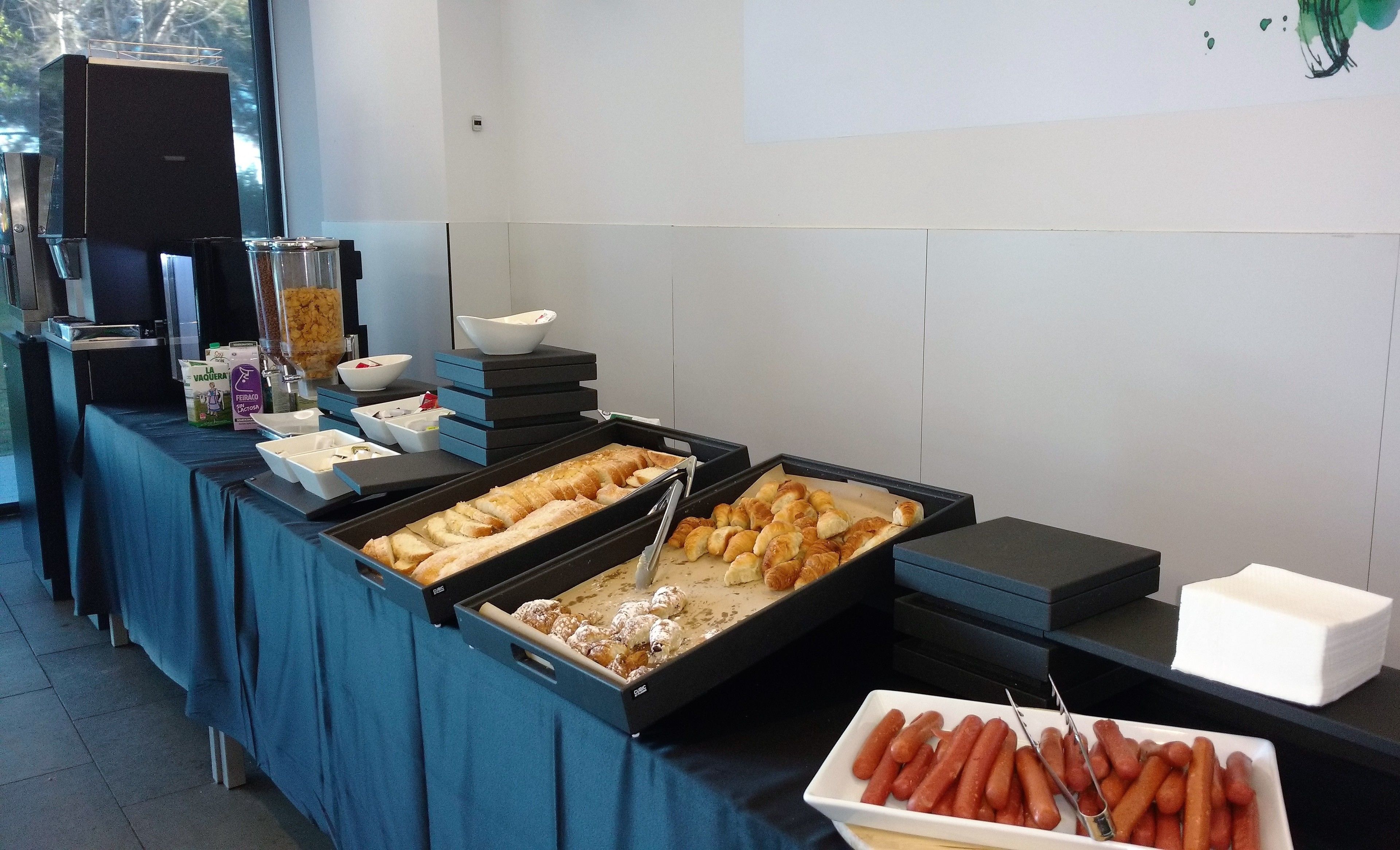 Uma mesa de buffet com diversos alimentos, incluindo pão, doces e cachorros-quentes.