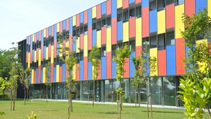 A modern building with a colorful facade, large windows, and a well-maintained lawn with young trees. - Centre Esplai Hostel (El Prat de Llobregat)