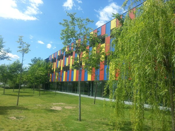 A modern building with a colorful facade, surrounded by a grassy area with trees.