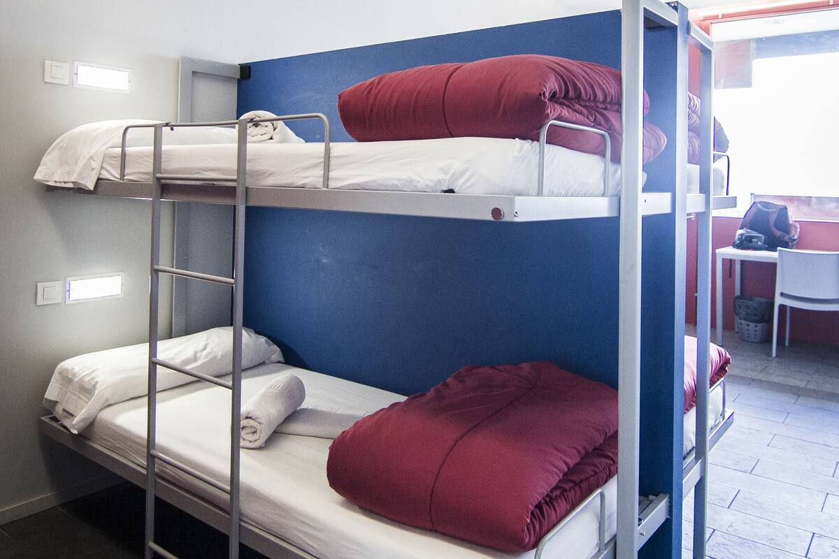 A bunk bed room with three levels, a desk, and a chair.
