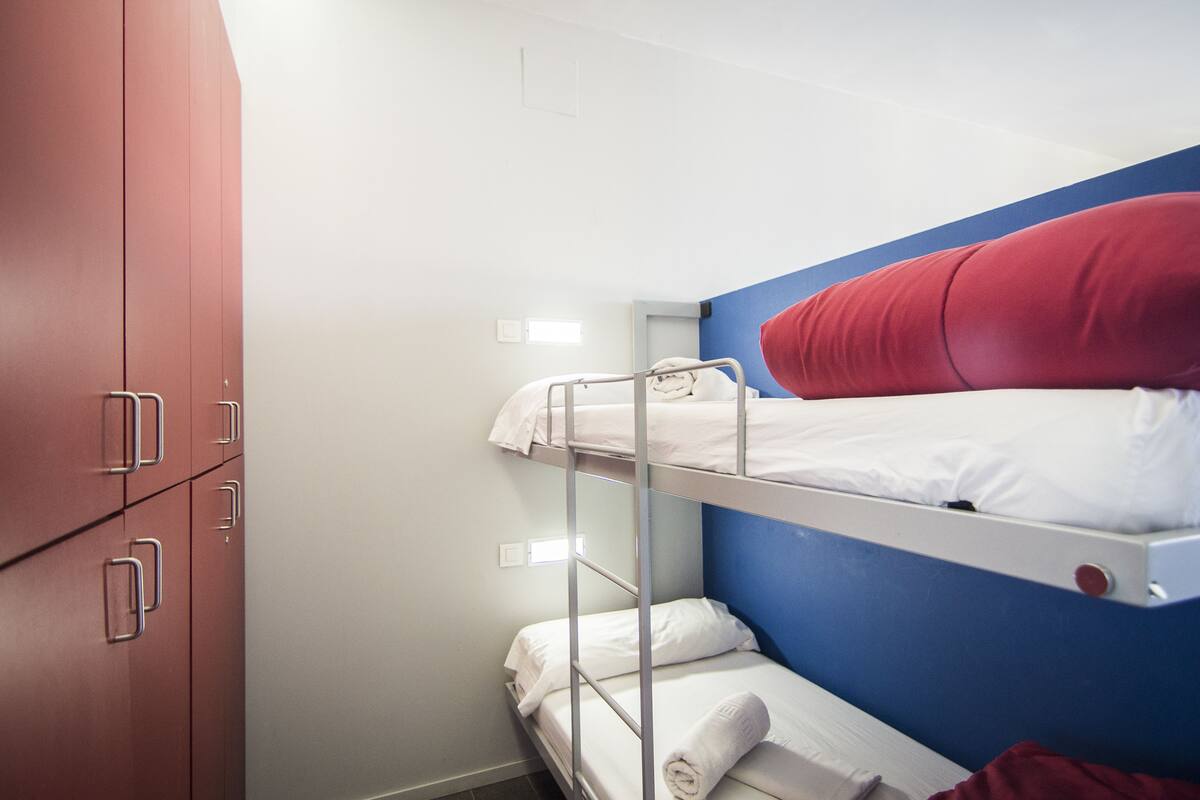 A bunk bed with white bedding and a red pillow, a red wardrobe, and a blue wall.