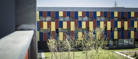 Un bâtiment moderne doté d’une façade colorée et d’une cour bien entretenue, agrémentée d’arbres et de sièges extérieurs.
