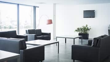 Un área de estar moderna y bien iluminada con asientos cómodos, un televisor de pantalla plana y ventanas amplias con vistas al exterior.