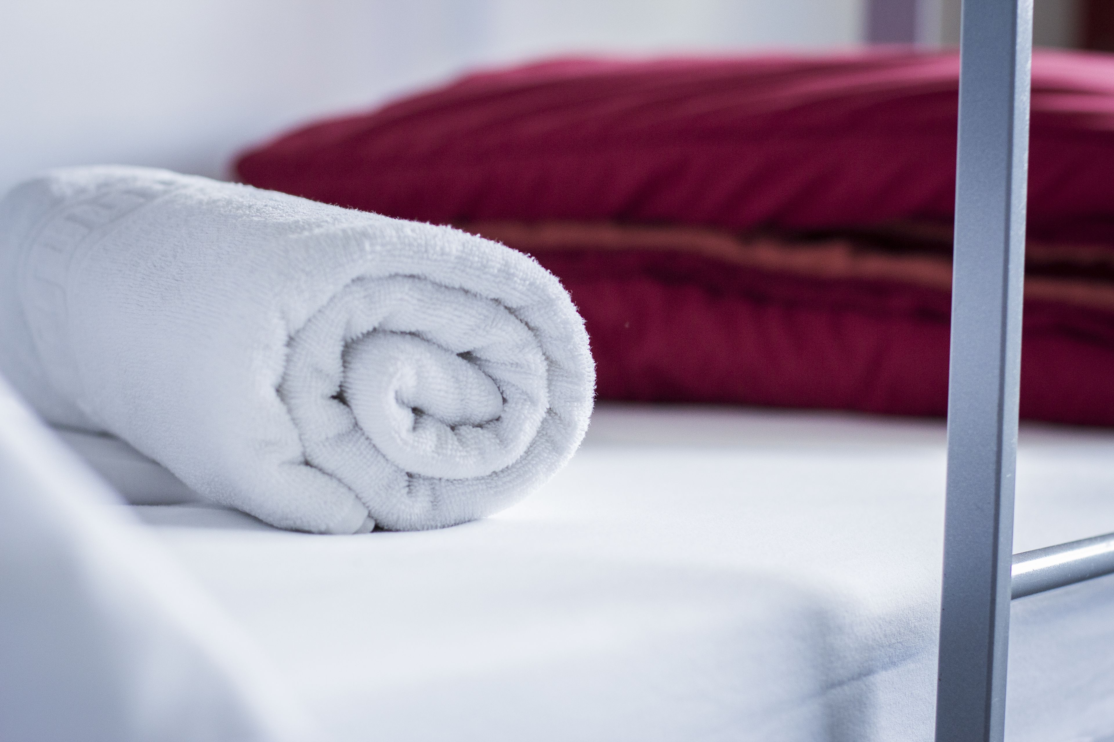 Una toalla blanca enrollada cuidadosamente sobre una cama con un cojín rojo.