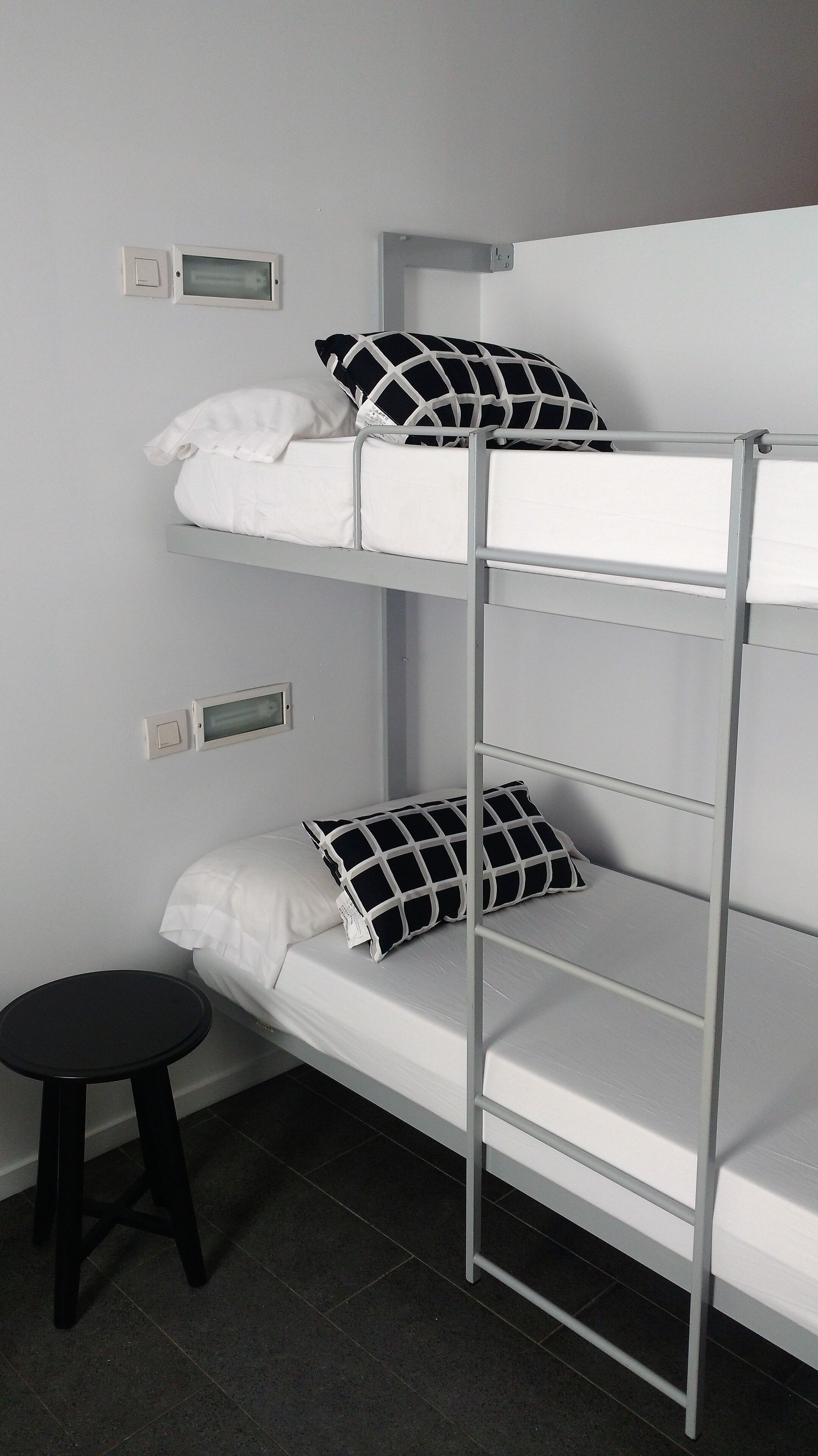 A bunk bed with two levels, each with a pillow and a control panel on the wall.