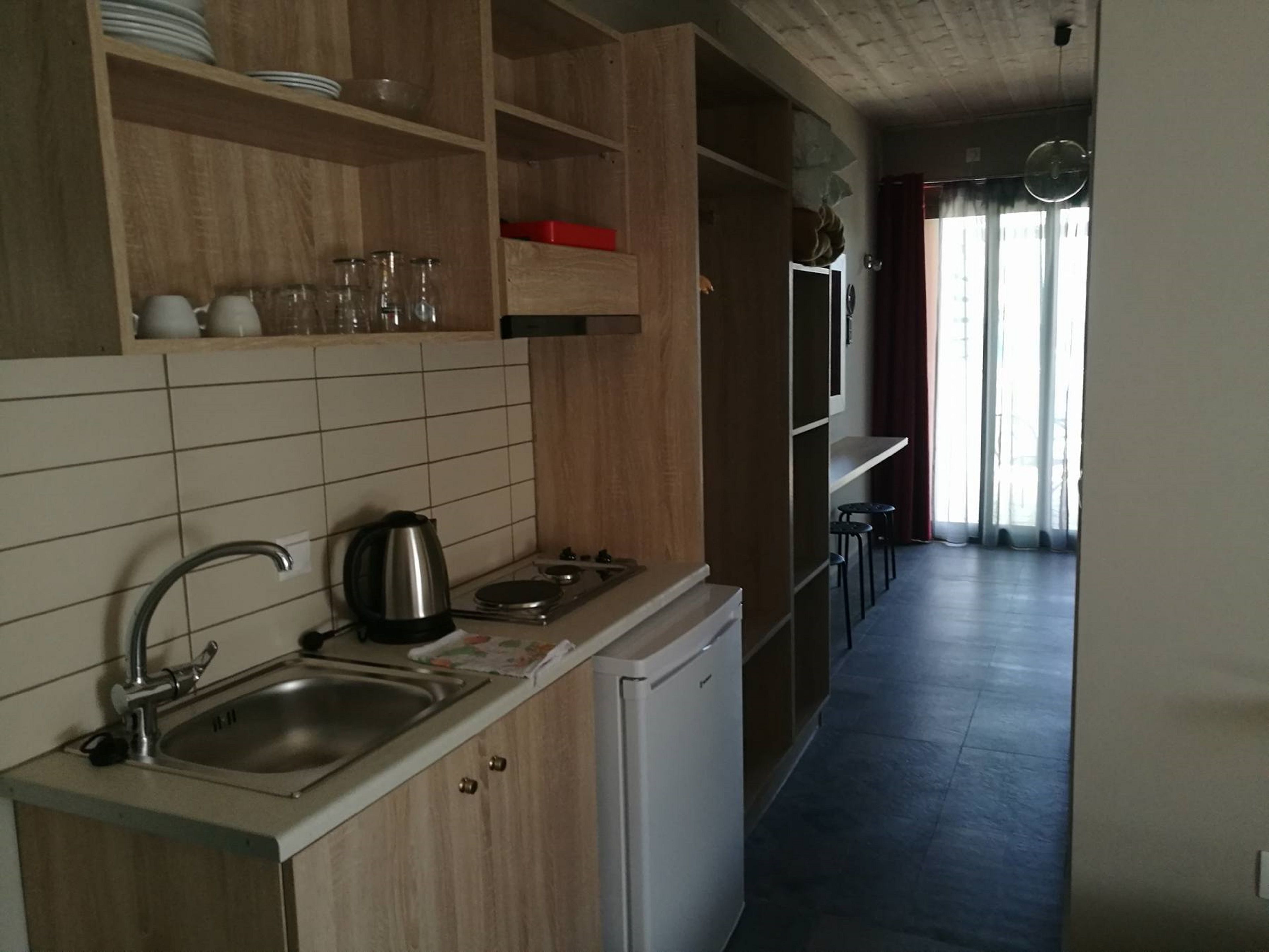 Eine Küche mit Spüle, Herd und Schränken. Ein Kühlschrank und ein Fenster mit Vorhängen sind ebenfalls vorhanden.