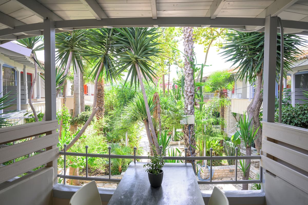 A covered patio with a table and chairs, surrounded by lush tropical plants and a view of a residential area.