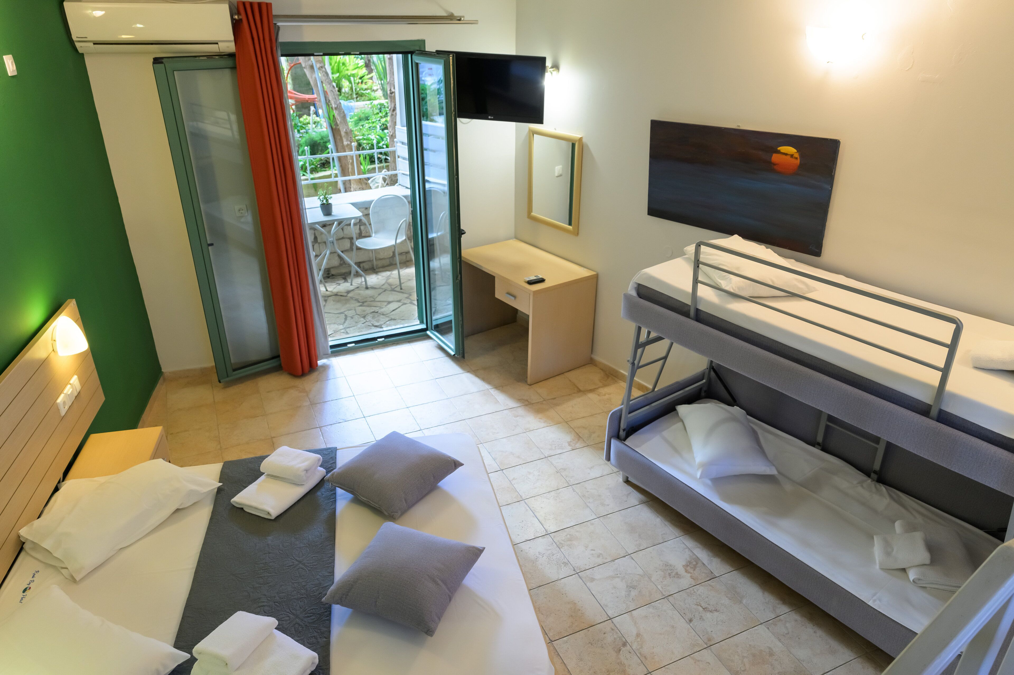 Une chambre d’hôtel comprenant un lit, un canapé-lit, un bureau, une chaise, un téléviseur et une porte-fenêtre coulissante donnant sur un espace extérieur.