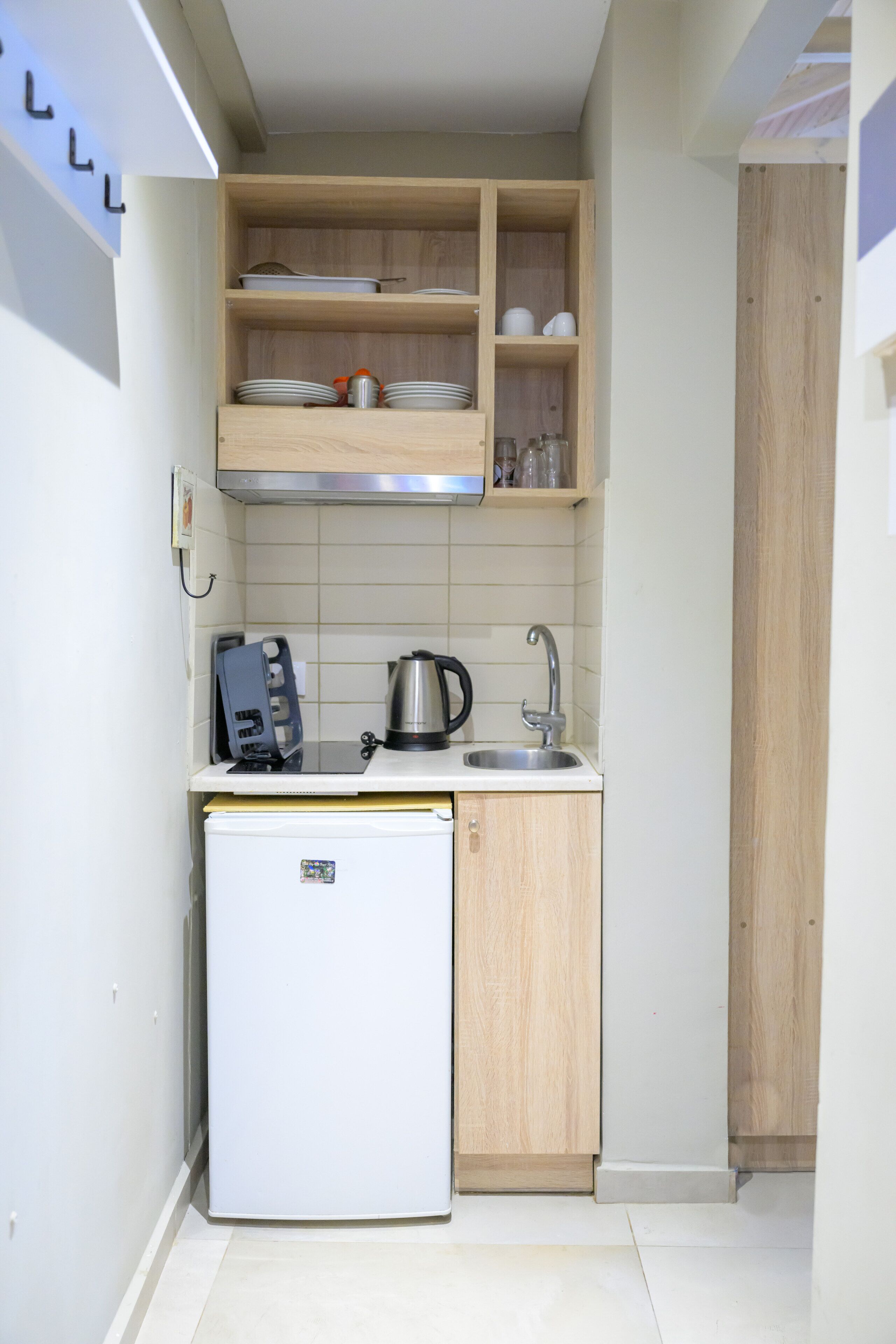 A compact kitchen with a built-in refrigerator, a sink, and wooden shelves above.