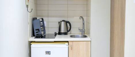 A compact kitchen with a built-in refrigerator, a sink, and wooden shelves above.