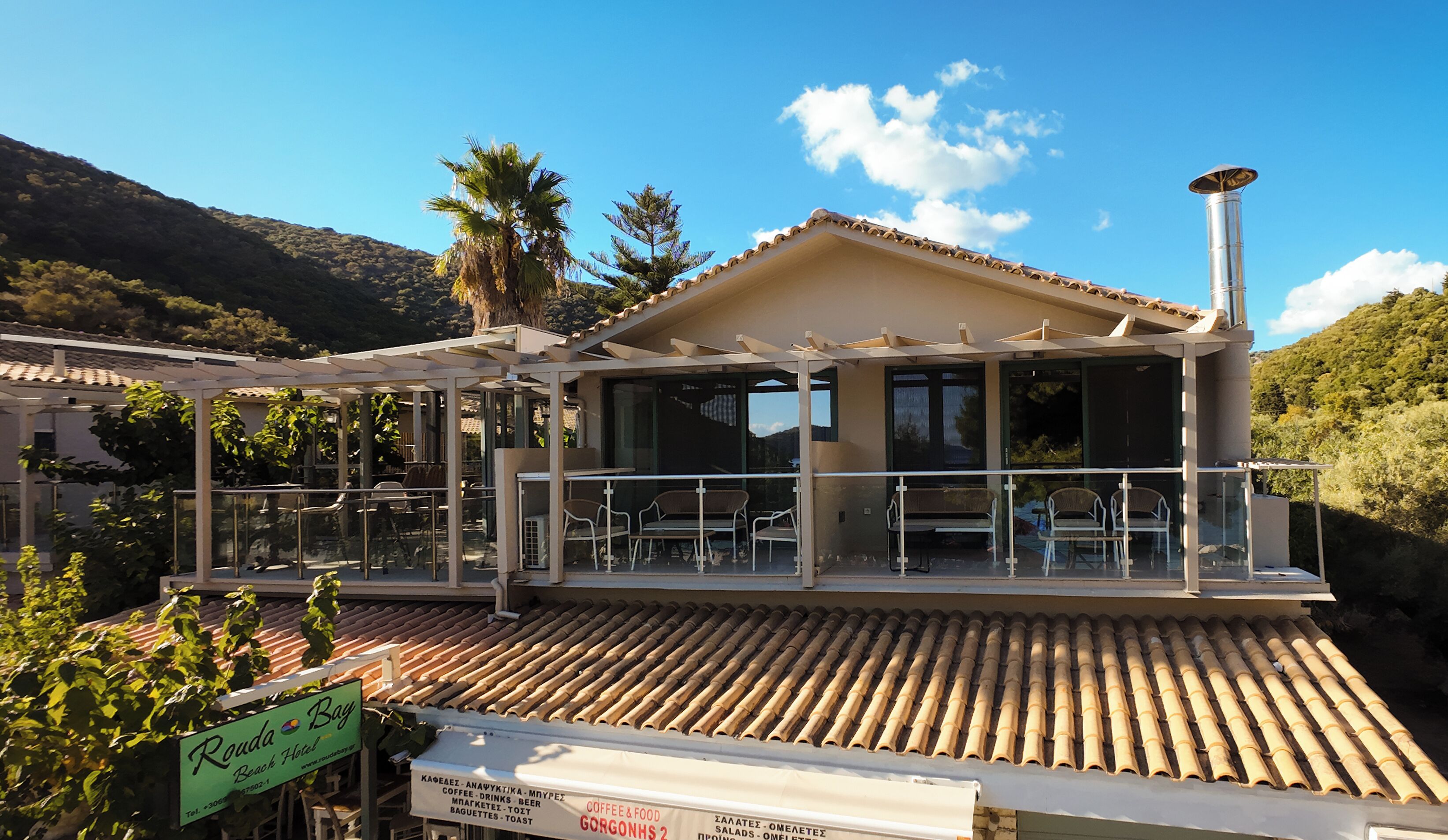 A beachside hotel with outdoor seating, a covered patio, and a sign indicating it is the Rouda Beach Hotel.