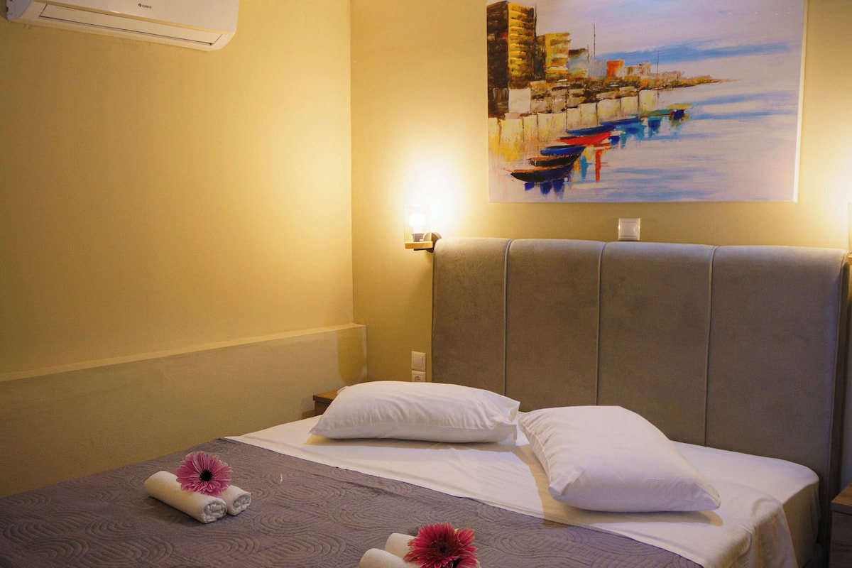 A hotel room with a bed, a painting on the wall, and an air conditioning unit.