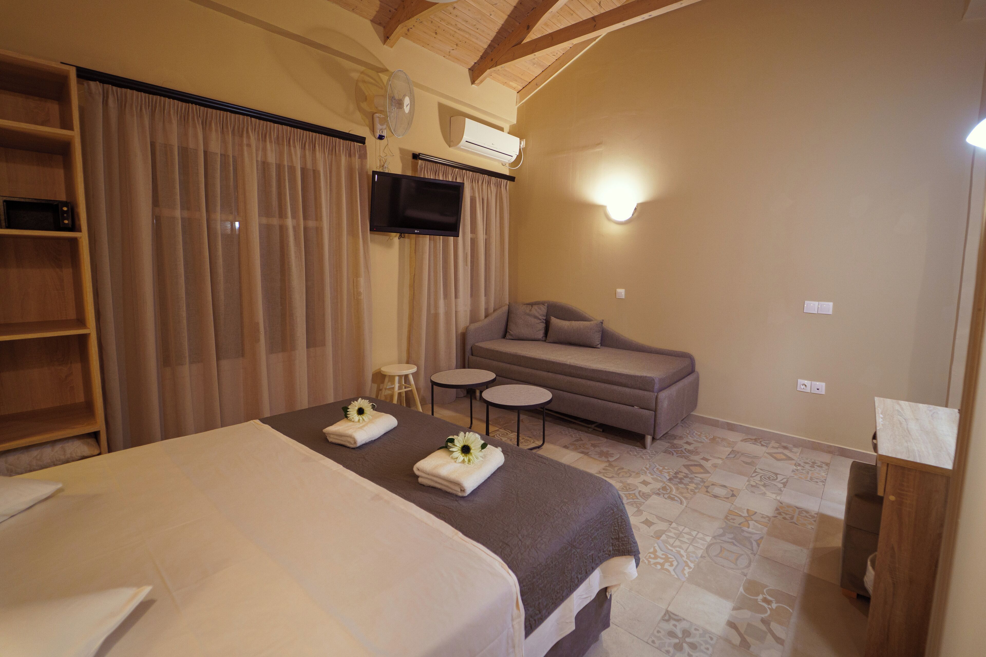 Ein Hotelzimmer mit einem großen Bett, einer Couch, einem Fernseher und einem Ventilator.