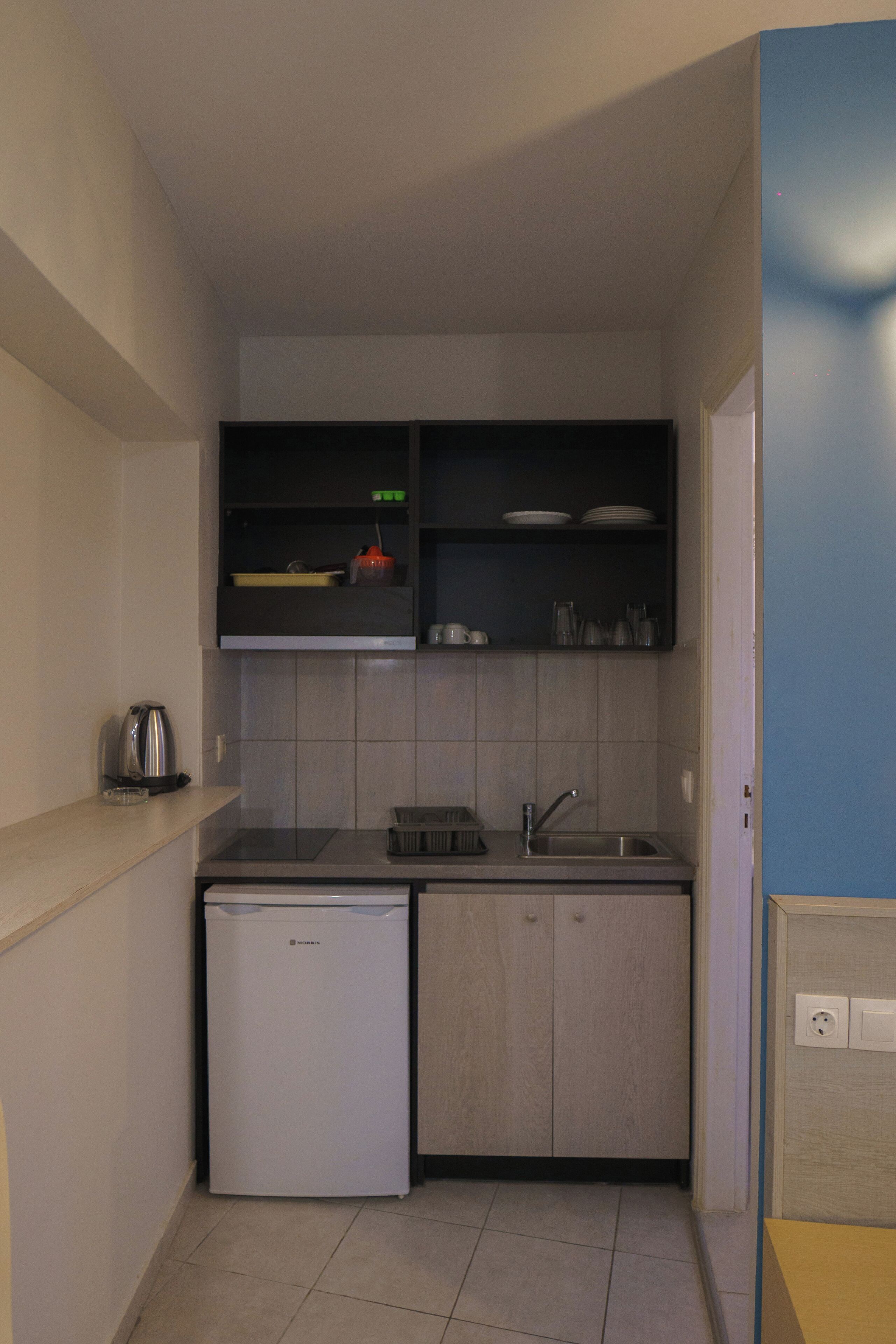 A compact kitchen with a dishwasher, sink, and shelves above the countertop.