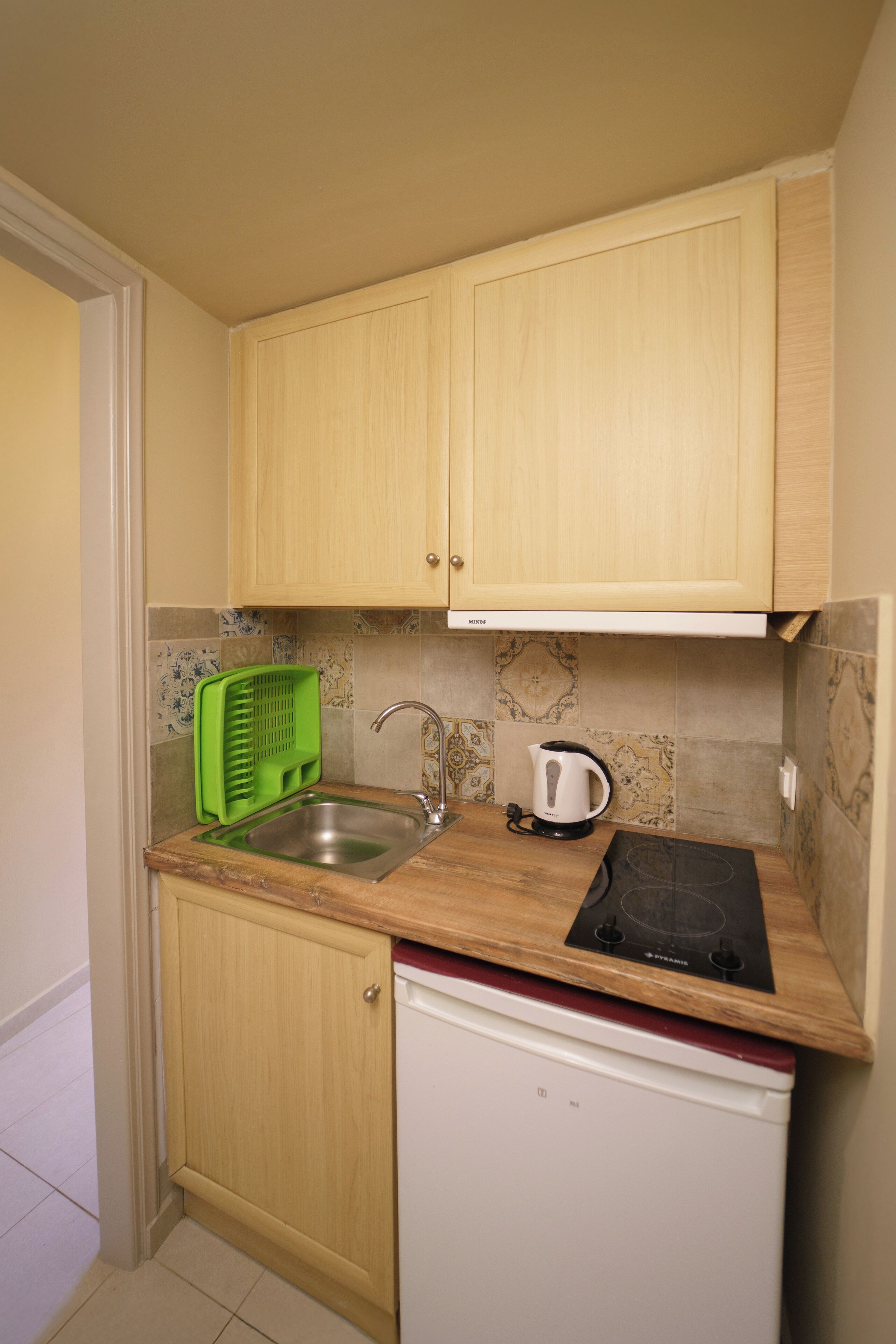 Eine kleine Küche mit Holzschränken, einer Edelstahl-Spüle, einem Wasserkocher und einem kleinen Kühlschrank.