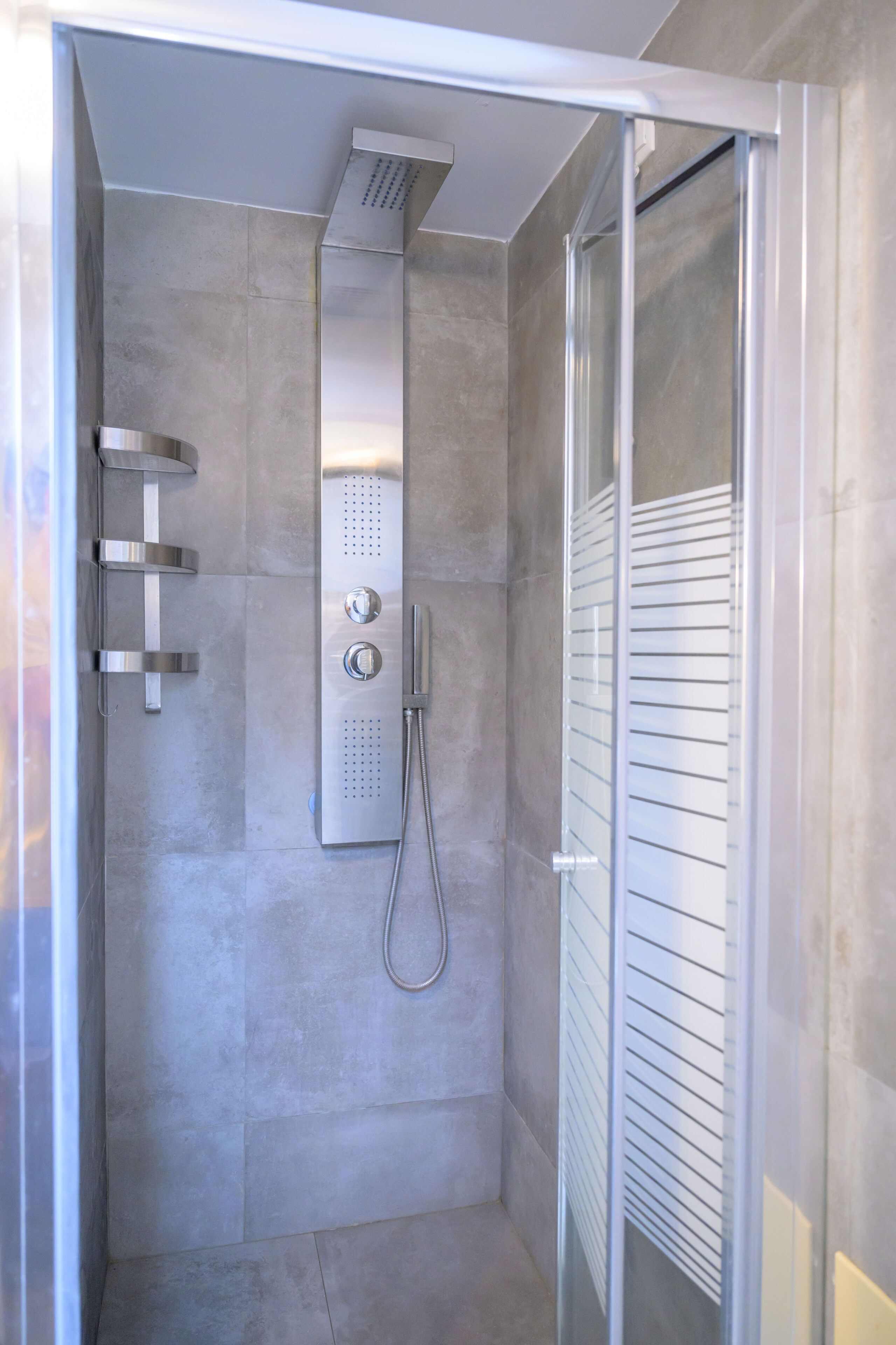 A modern shower with a glass door, a handheld showerhead, and a wall-mounted control panel.