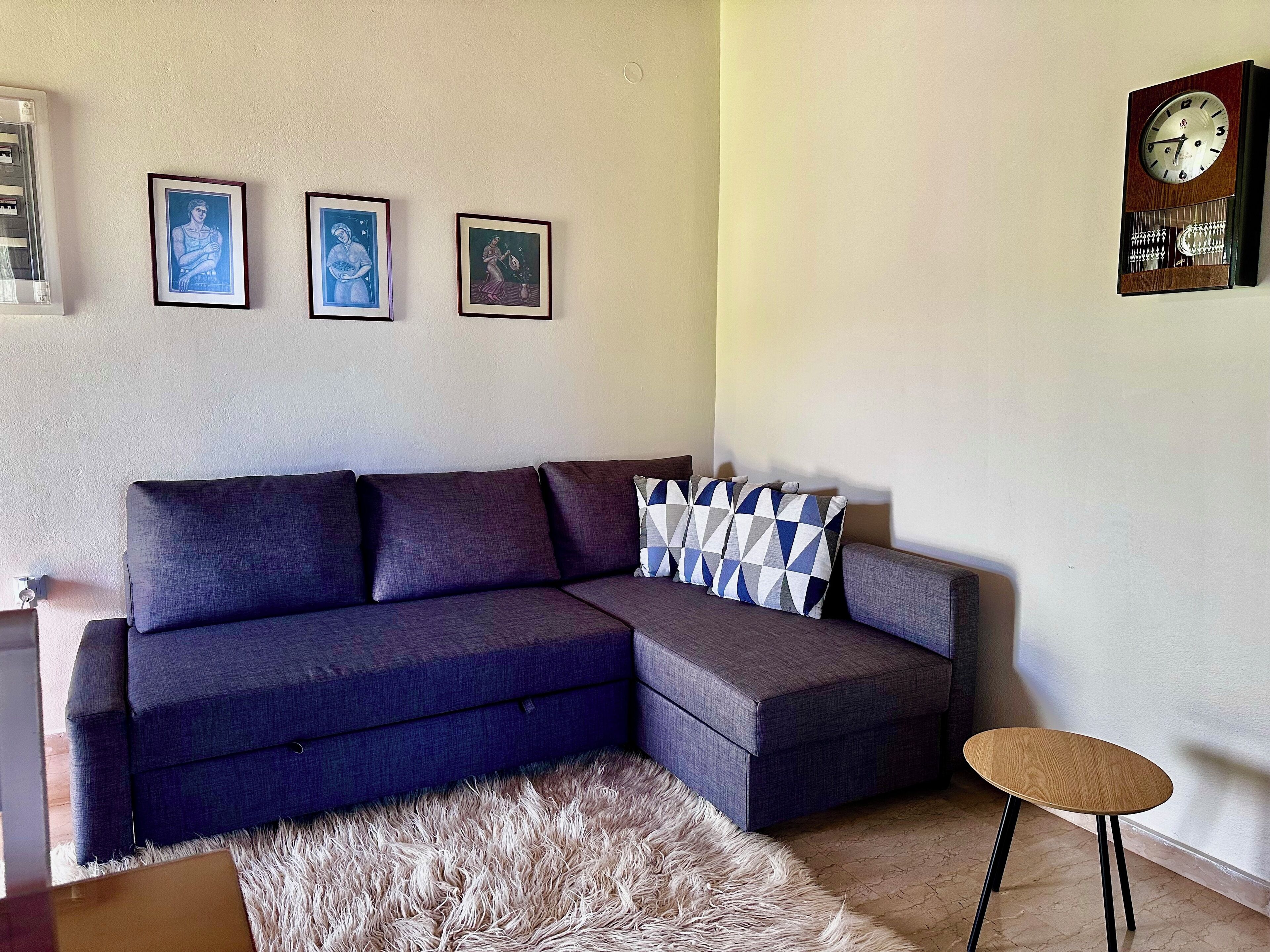 A living room with a sectional sofa, a small round table, a shaggy rug, and three framed pictures on the wall.