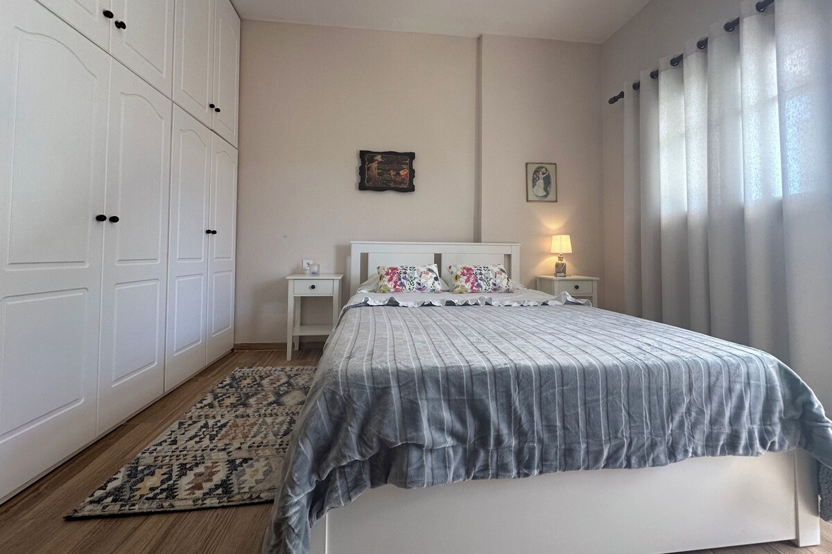 Quarto com cama, mesas de cabeceira, abajur, tapete, guarda-roupa e luminária no teto.