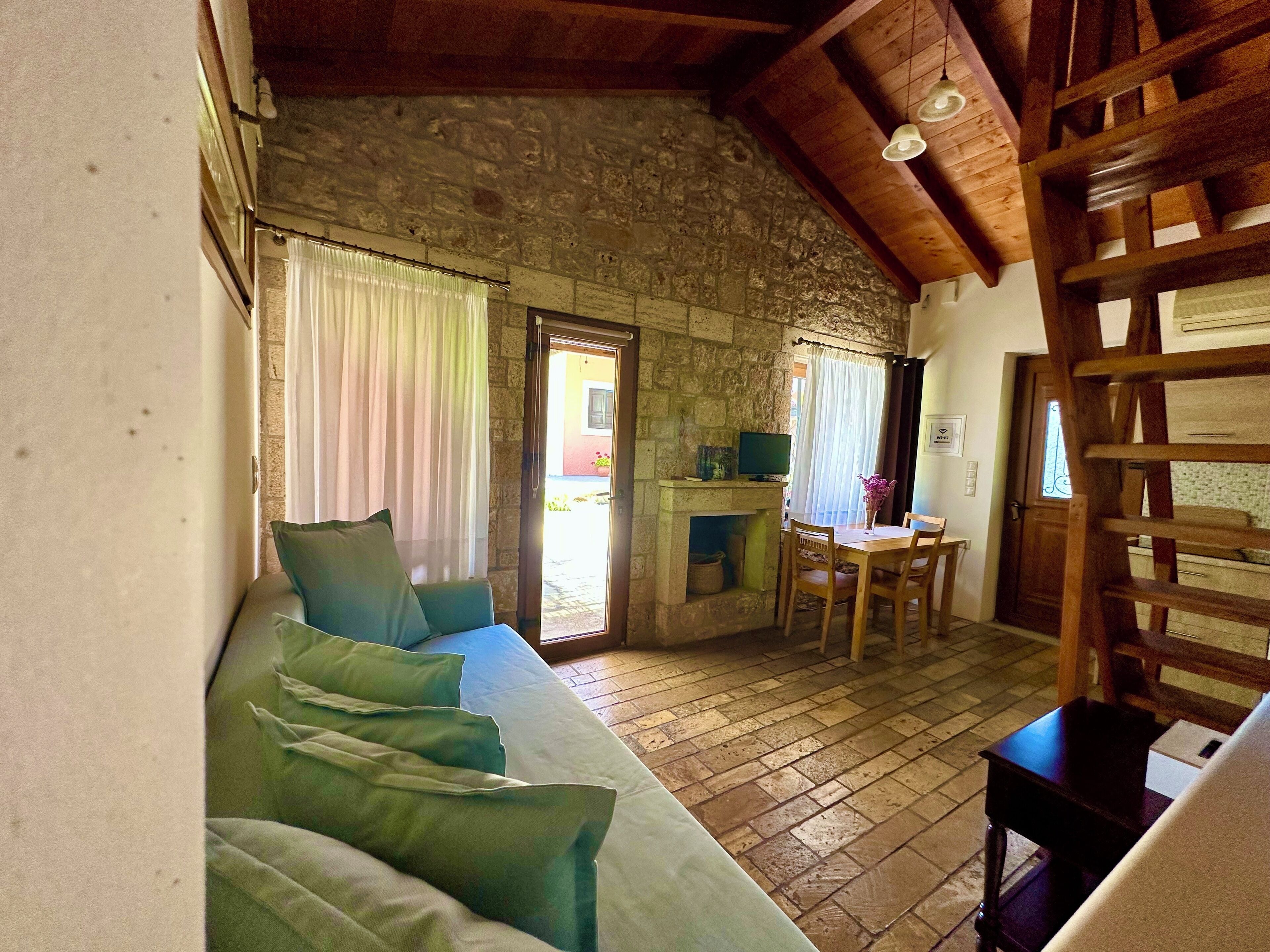 Une pièce chaleureuse avec un mur en pierre, un plafond en bois, un canapé avec des coussins, une petite table et une cheminée.