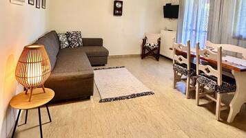 Una sala de estar acogedora con techo de madera, un sofá, una mesa con sillas, una lámpara y cuadros enmarcados en la pared.