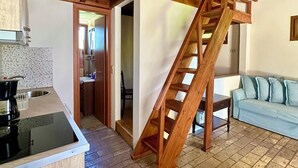 Un interior rústico con vigas de madera a la vista, una escalera, una cocina con estufa y un sofá azul.