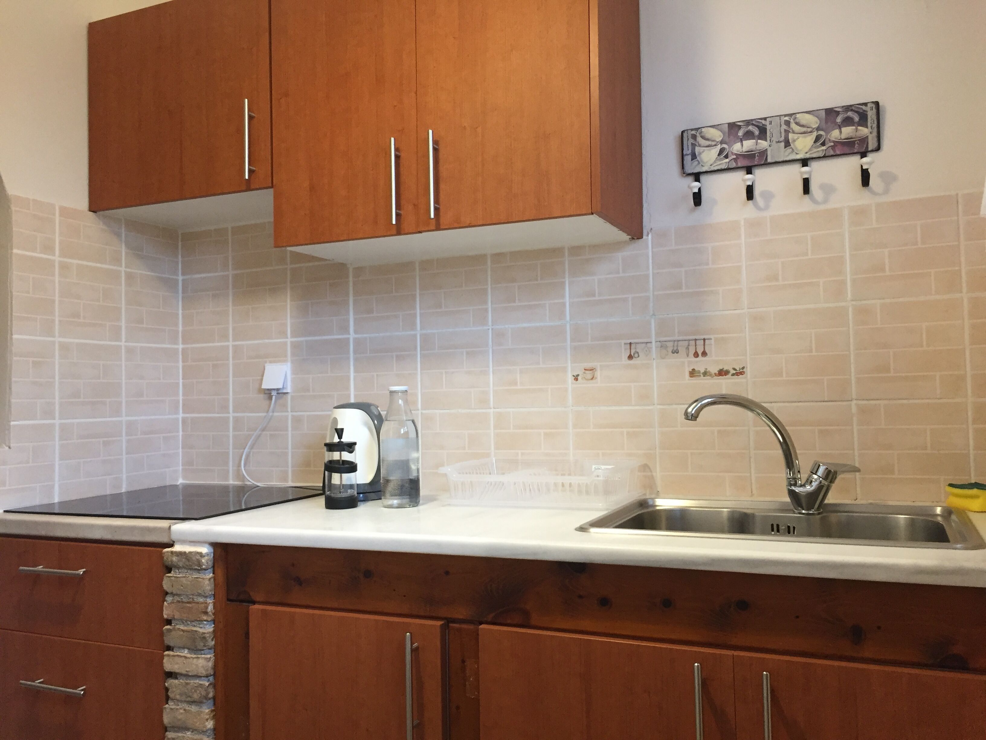A kitchen with wooden cabinets, a stainless steel sink, a coffee maker, and a tiled backsplash.