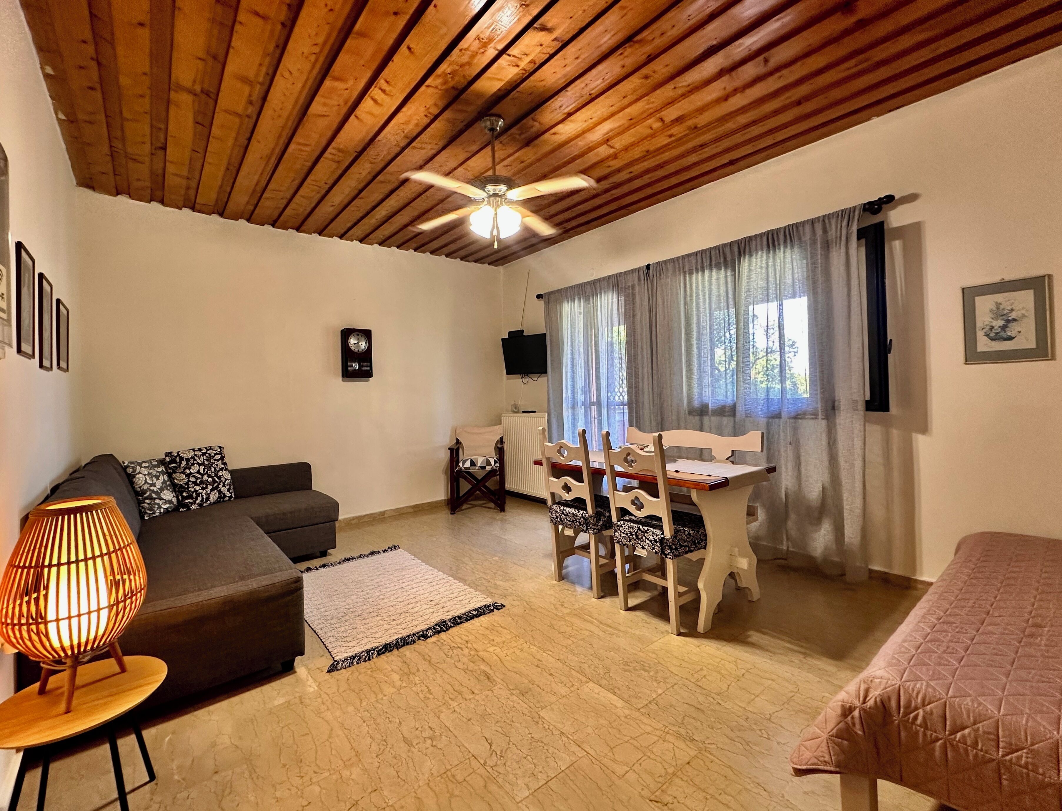 Una sala acogedora con techo de madera, un sofá, una mesa de comedor con sillas, un televisor y una cama.