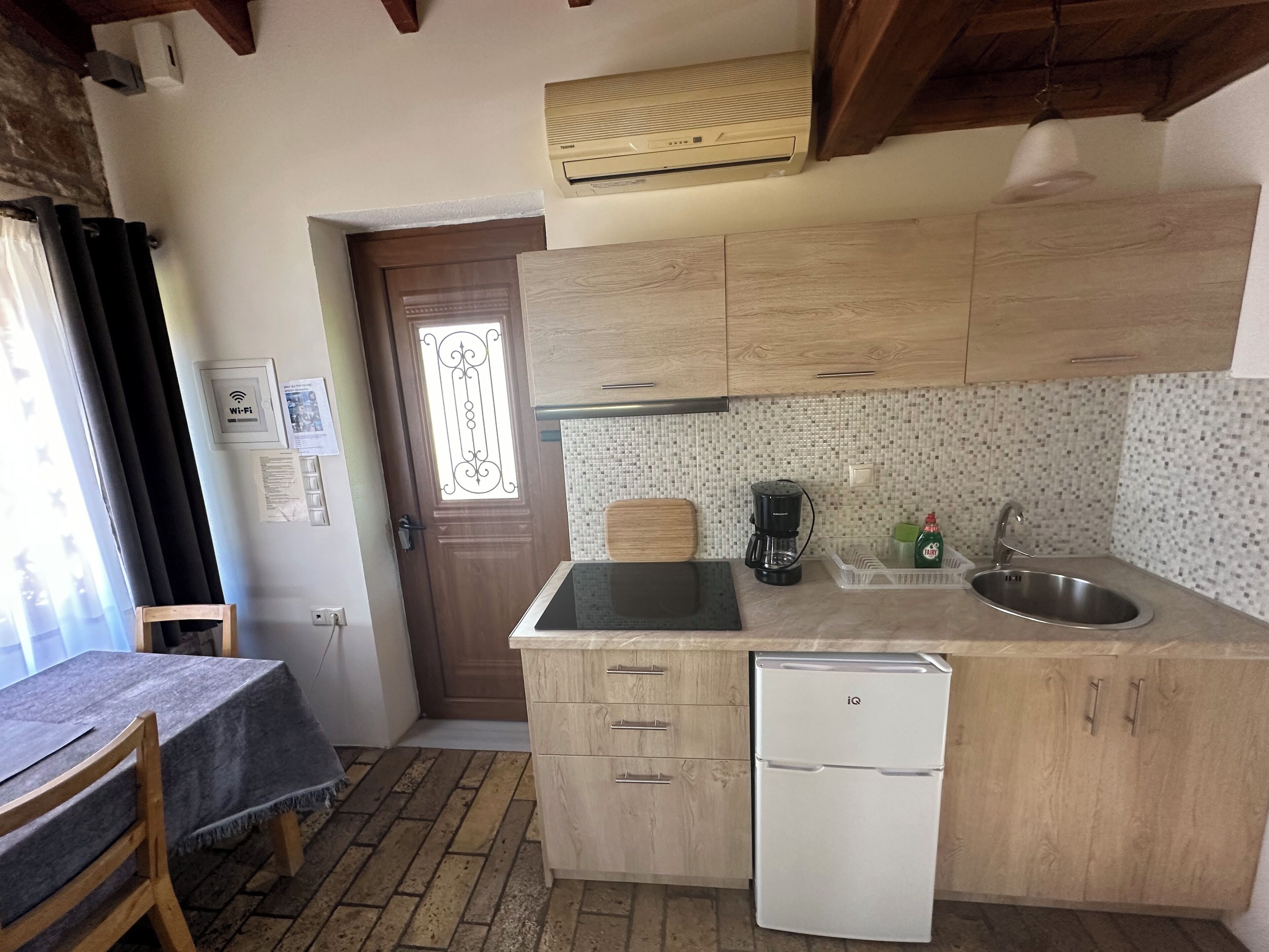 Una cocina compacta con armarios de madera, lavavajillas integrado, cafetera y fregadero.