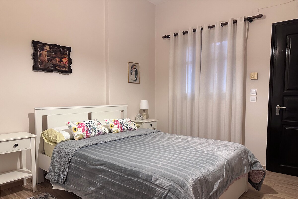 Un dormitorio con cama, mesitas de noche, lámpara, un cuadro enmarco y una puerta.