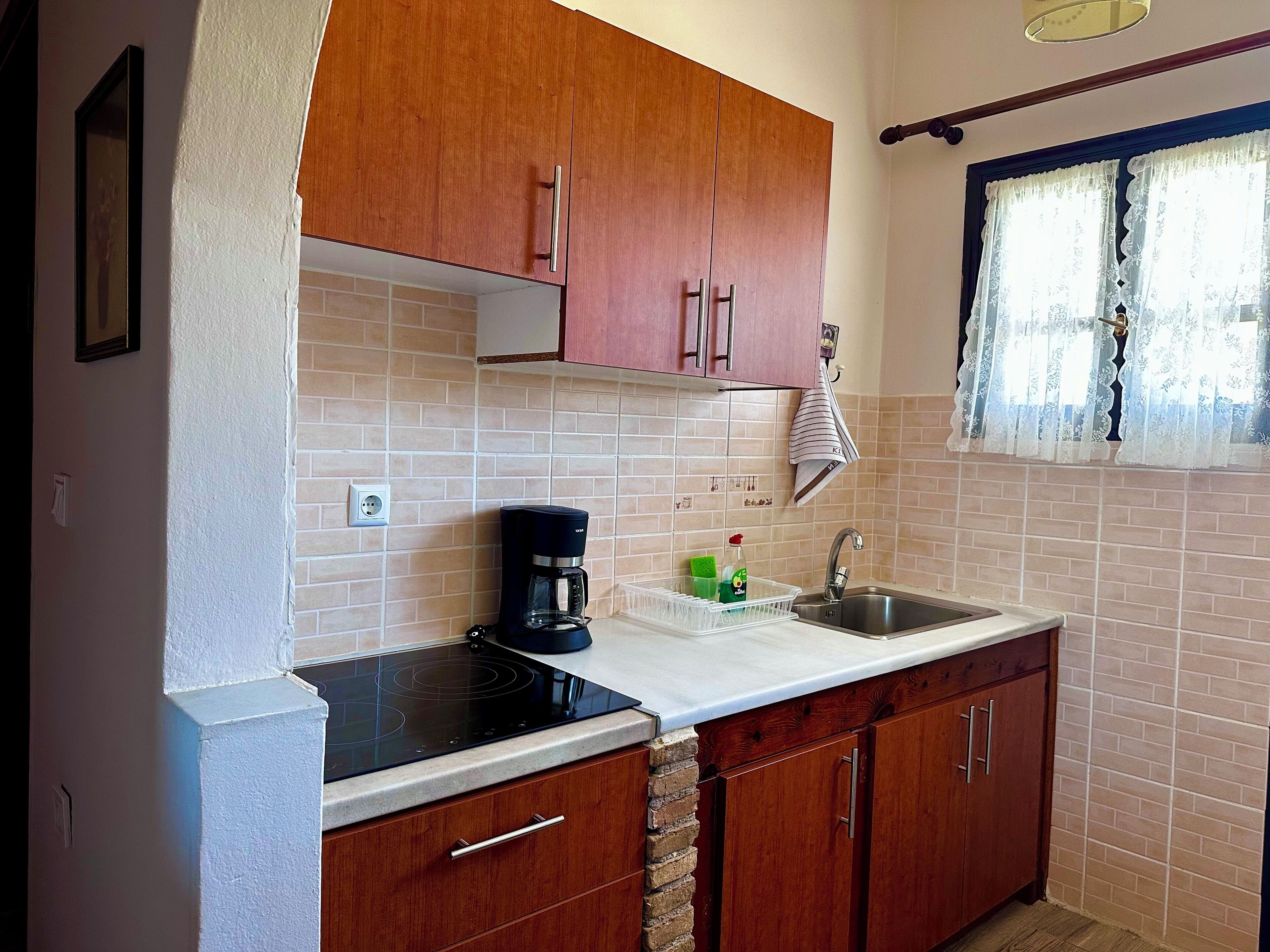 Una cocina con armarios de madera, una estufa negra, un fregadero y una ventana con cortinas de encaje.