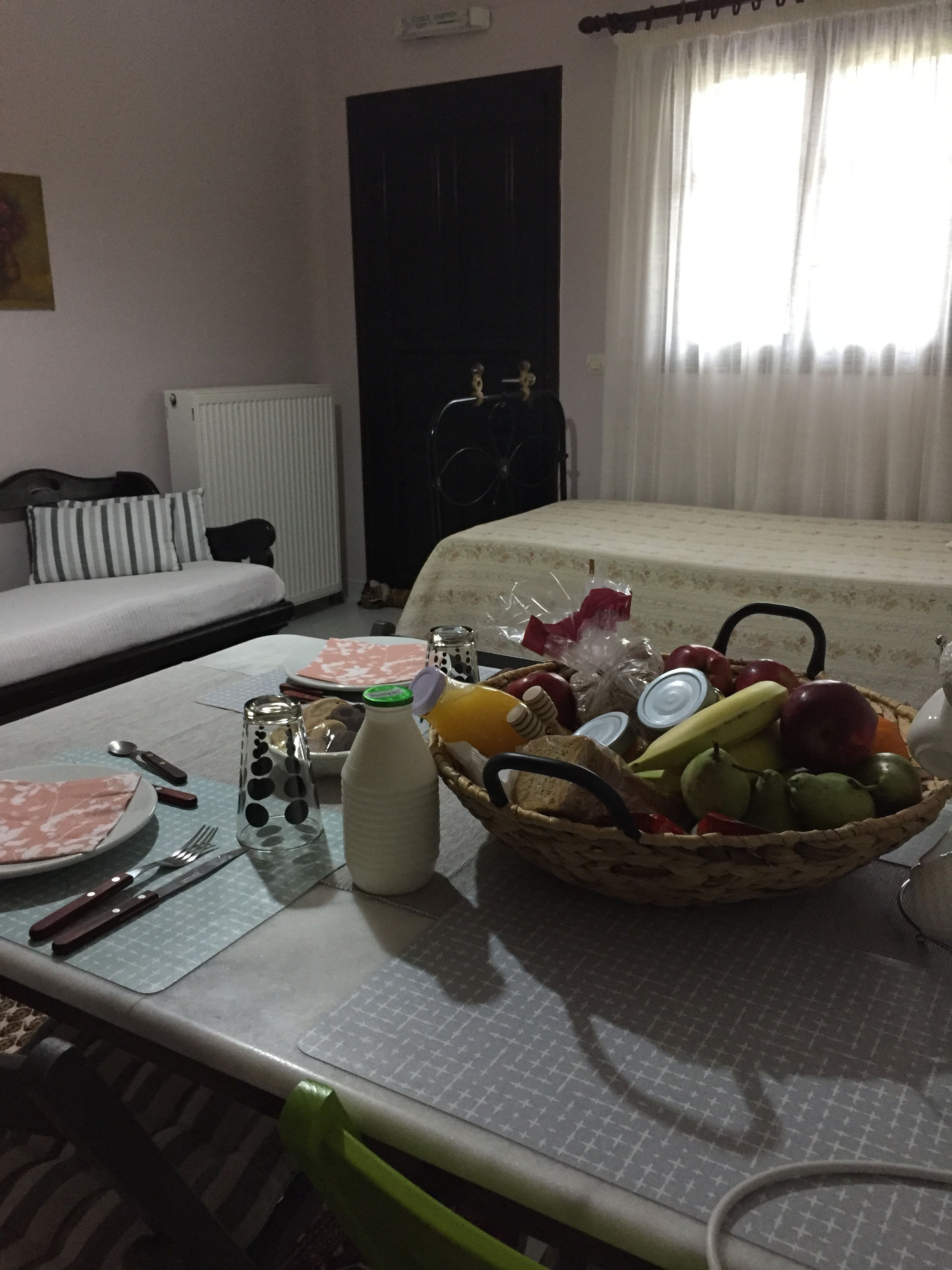 A neatly arranged dining area with a table set for two, including plates, cutlery, a bottle, and a basket of fruit.