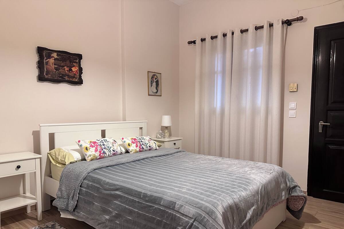 A bedroom with a bed, bedside tables, a nightstand, a lamp, a framed picture, and a door.