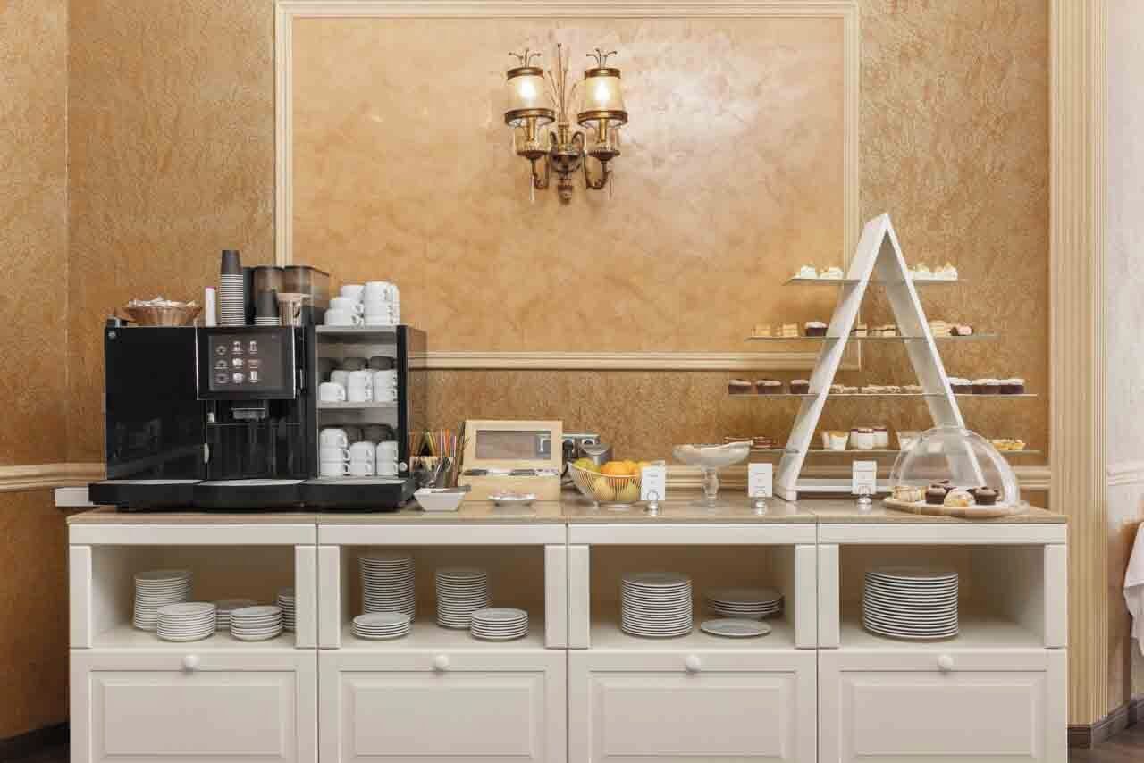 Disposición de un bufé con una máquina de café, platos, tazones y una mesa de postres.