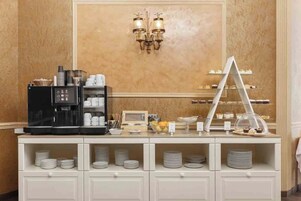 Disposición de un bufé con una máquina de café, platos, tazones y una mesa de postres.