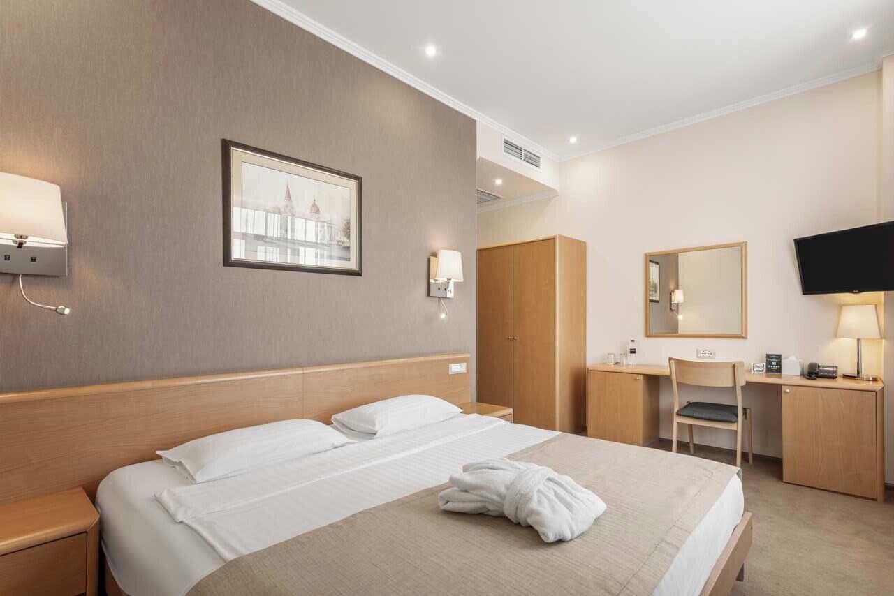 A hotel room with a bed, bedside table, wardrobe, desk, chair, and a television.