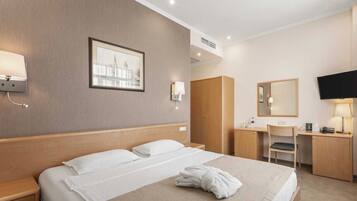 A hotel room with a bed, bedside table, wardrobe, desk, chair, and a television.
