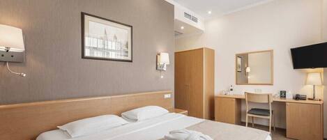A hotel room with a bed, bedside table, wardrobe, desk, chair, and a television.