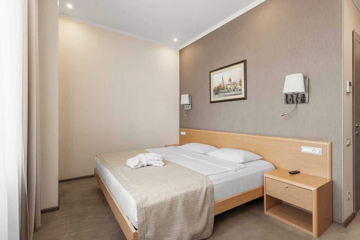 A hotel room with a bed, bedside table, lamp, and a painting on the wall.