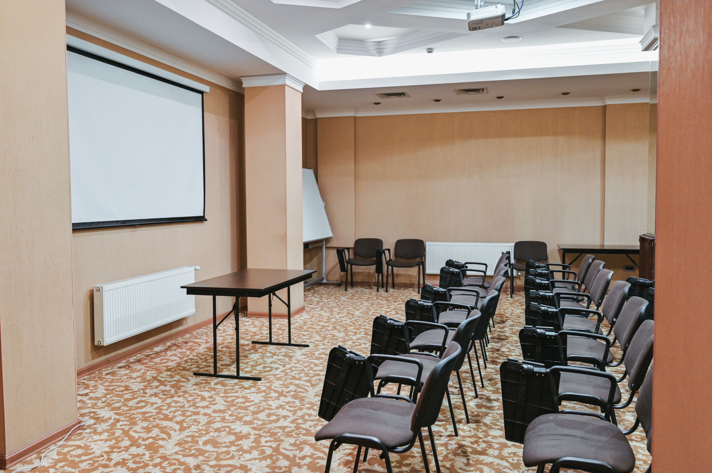 A conference room with a projector screen, a whiteboard, and rows of chairs.