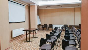 A conference room with a projector screen, a whiteboard, and rows of chairs.