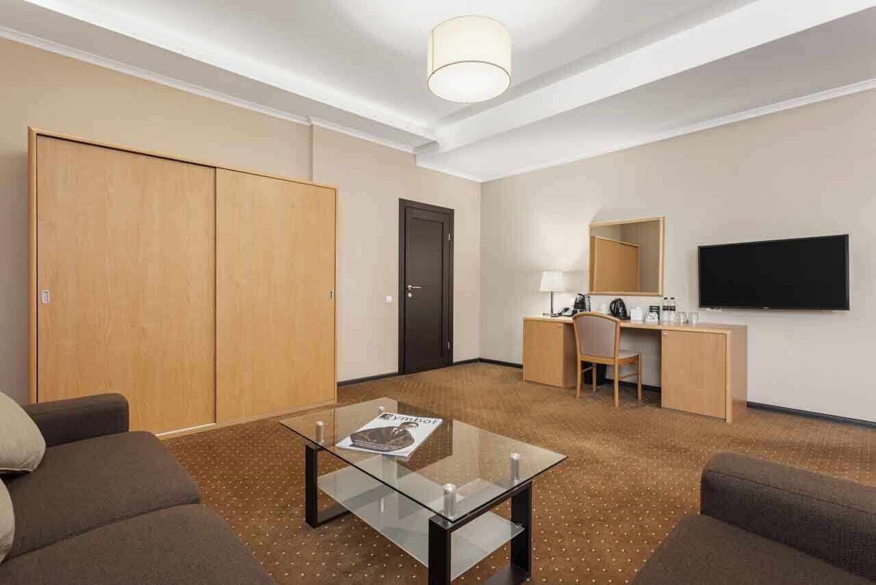 Habitación de hotel con sofá, una mesa de centro de vidrio, escritorio con silla, televisión y armario.