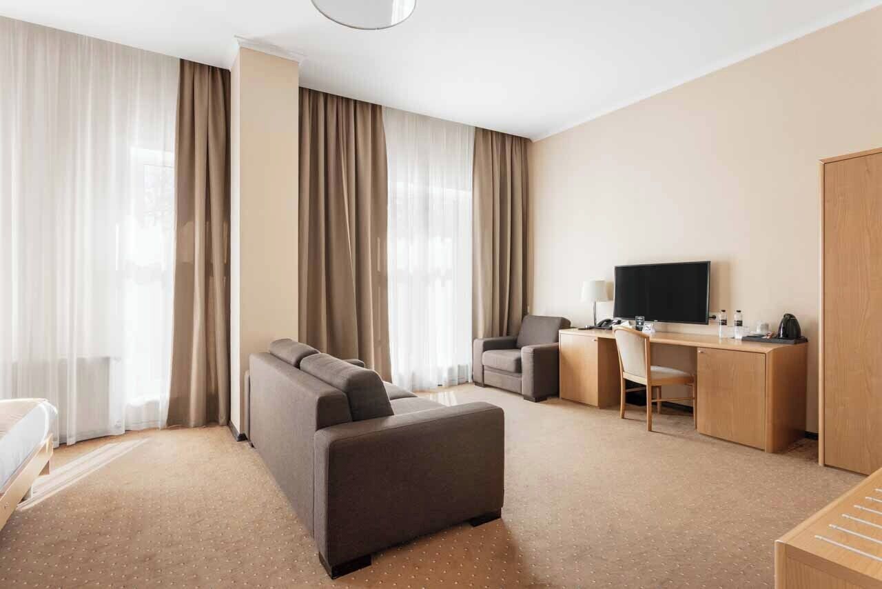 A hotel room with a bed, a sofa, a desk, a chair, a television, and curtains.