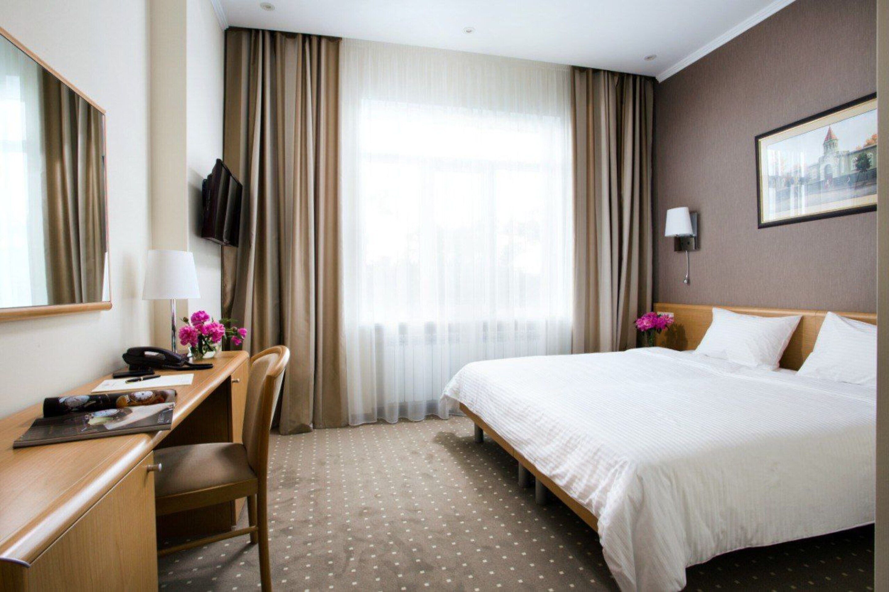 Hotelkamer met een bed, bureau, stoel, televisie en raam met gordijnen.