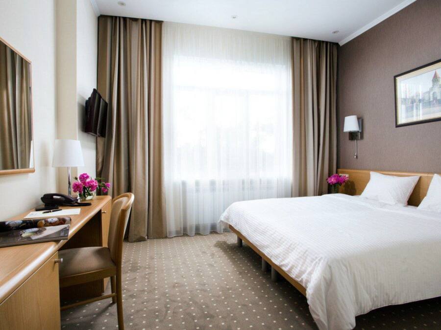 Hotelkamer met een bed, bureau, stoel, televisie en raam met gordijnen.