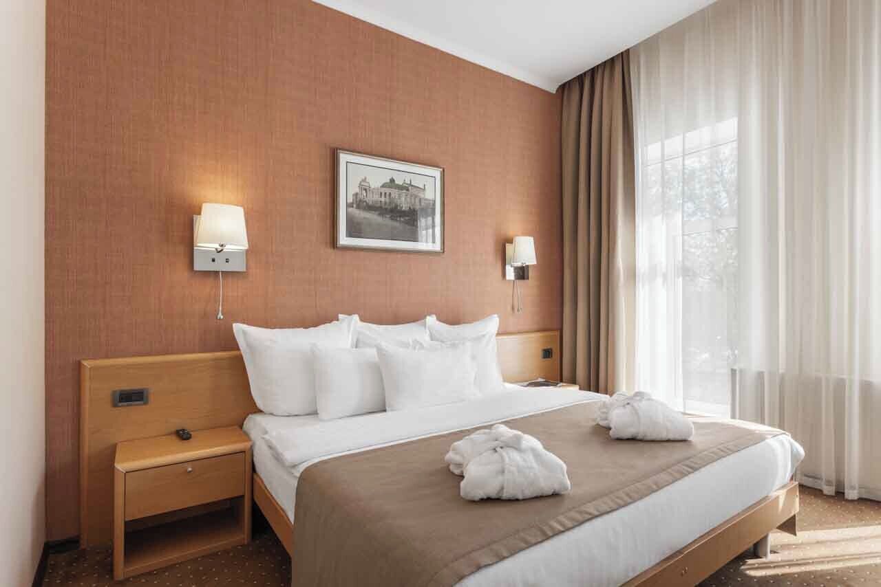 Una habitación de hotel con una cama, dos mesitas de noche, un cuadro colgado en la pared y una ventana con cortinas.