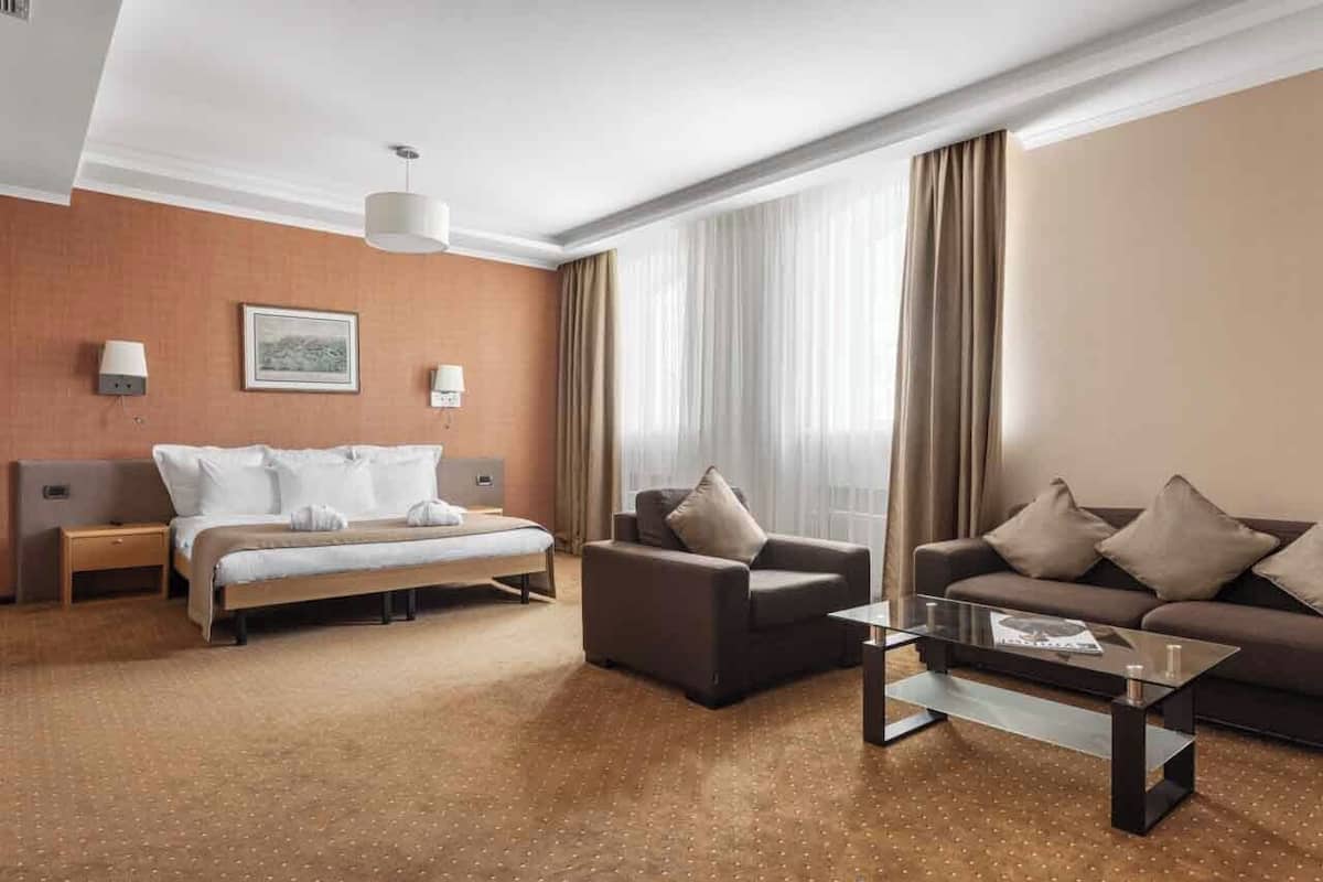 A hotel room with a bed, two sofas, a coffee table, a lamp, and a large window with curtains.