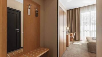 A hotel room with a wooden bench, a desk, a bed, and a large window with curtains.